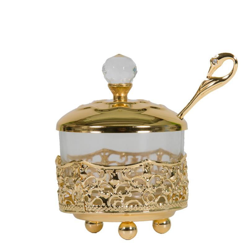 A small glass honey dish in a decorative gold filigree holder with matching gold lid and spoon, displayed on a white background.