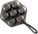 The image displays a cast iron aebleskiver pan. It's a dark-colored pan with a single handle and seven hemispherical indentations, which are used to cook aebleskiver (Danish pancake balls). The shape of the pan, excluding the handle, is hexagonal.