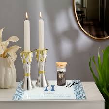 Two elegant silver candle holders with white candles, a decorative jar, and a plant, all set on a stylish table with a mirror in the background.