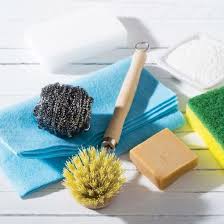 A collection of cleaning supplies including sponges, scrubbers, a dish brush, and bars of soap on a white surface.