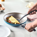 Farberware 15-Piece Aluminum Nonstick Cookware Set in a teal exterior with a light gray nonstick interior. The set includes various pots and pans with glass lids and black handles, along with a baking sheet and a set of black Prestige kitchen tools shown in an inset image.