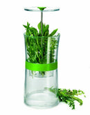 A large, clear herb keeper filled with a variety of fresh green herbs, including sage and rosemary. A green band wraps around the middle, and the base holds water to keep the herbs hydrated.