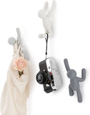Set of three grey Umbra Buddy wall hooks shaped like climbing figures, used to hang a bag and a camera, shown on a white background.