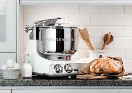 A stand mixer with a stainless steel mixing bowl, whipping batter with a beater attachment.
