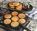 Black round pancake pan with seven circular molds and a black handle.