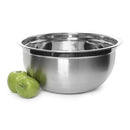 Large stainless steel mixing bowl with a reflective finish, placed on a white surface. Two green apples rest beside the bowl.