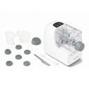 A white Starfrit electric pasta maker extruding long strands of fresh pasta. The machine has a clear top allowing a view of the dough inside. To the left, a white plate of cooked spaghetti with tomato sauce and shrimp is shown as a serving suggestion.