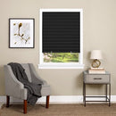 Black pleated window shade installed inside a white window frame. The shade is fully extended, blocking light while allowing a small view of a green outdoor landscape. Simple and modern design for privacy and light control.