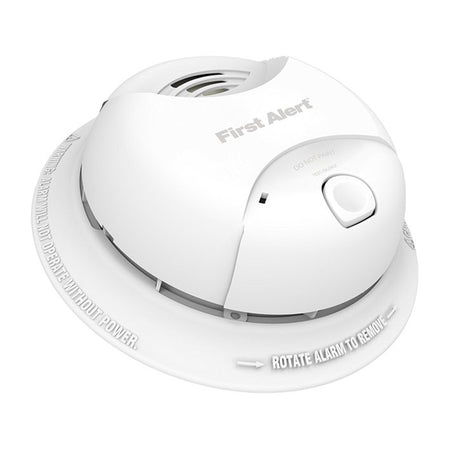 A First Alert smoke detector with a sleek white design. The device features a central test/silence button, vent openings for smoke detection, and embossed text around the base instructing users to 'Rotate Alarm to Remove' and warning that the alarm will not operate without power.