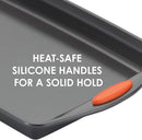 A gray 10" x 15" Rachael Ray nonstick cookie sheet with orange silicone grip handles shown on a white background.