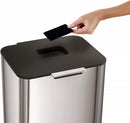 A two-tiered stainless steel trash and recycling bin with a black lid and base. The top compartment has a small, horizontal orange light on its front.