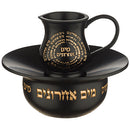 A black, two-piece Jewish ritual washing cup set with gold Hebrew text. The set includes a handled pitcher and a matching bowl designed to collect water.