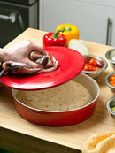 A round, red stoneware tortilla warmer with a ribbed texture, a matching lid, and a small round knob handle.