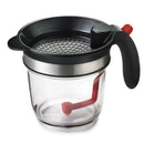 Clear fat separator with black handle and strainer, and a red stopper inside.