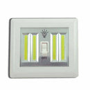 A rectangular, white wireless LED light switch with a toggle switch in the center. It has two vertical panels of bright LED lights.