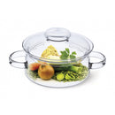 A clear 2-liter round glass casserole dish with a lid. The dish contains raw ingredients for a soup or stew, including an onion, carrot, leek, celery, a bunch of parsley, and green lentils.