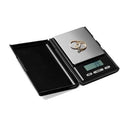 A small, black and silver digital pocket scale with a black protective cover.

