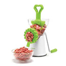 A manual meat grinder with a white base and a green handle. It is shown grinding pieces of meat into a clear bowl.