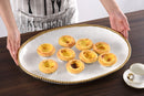 Tarts neatly aligned on a White porcelain oval serving platter with a gold beaded rim displayed on a wooden table