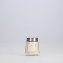 A small, clear glass jar candle with a light beige wax. It has a silver metal lid and a decorative label with the scent "Bella Fresia."