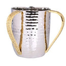 A stainless steel washing cup (Netilat Yadayim) with a bright hammered finish on the body and two upright, textured gold-colored handles.