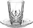 A clear, cut-style crystal Kiddush cup with a diamond and starburst pattern on its lower half. The cup rests on a small, matching crystal saucer with a fluted edge.