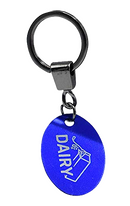 A close-up shot of a single keychain. It features a metal keyring and a smaller ring from which a blue, oval-shaped tag hangs. The tag is engraved with the word "DAIRY" and an image of a cow.
