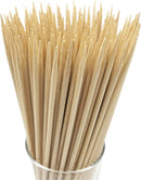 A bundle of natural bamboo skewers with pointed tips, neatly arranged in a clear glass container. The skewers are light beige in color and appear smooth and sturdy, ideal for grilling, kabobs, or food preparation.