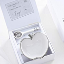 A white ceramic bowl shaped like an apple with a silver rim and stem, accompanied by a white ceramic spoon with silver bands on the handle. Dimensions for the bowl (5" x 4.5" x 2.5") and spoon (5" long) are indicated.