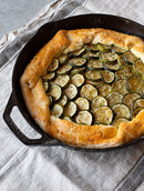 Black cast iron skillet with a long ergonomic handle and helper handle, featuring a smooth cooking surface and dual pour spouts.