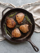 Black cast iron skillet with a long ergonomic handle and helper handle, featuring a smooth cooking surface and dual pour spouts.