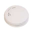 An image of a First Alert Smoke and Carbon Monoxide Alarm, a round, white device with a prominent "First Alert" logo and text reading "SMOKE AND CO ALARM." It features a central circular button or vent with a rectangular opening on the left and a narrow slit on the right. The device is shown at a slight angle against a plain white background.