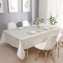 White and silver jacquard tablecloth covering a large dining table in a bright indoor setting with minimal tableware.