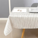 White and silver jacquard tablecloth covering a large dining table in a bright indoor setting with minimal tableware.