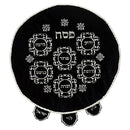 A round, black velvet matzah cover with intricate silver embroidery. The design features the Hebrew word 'Pesach' and six labeled compartments for Seder foods.