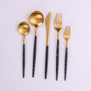 Modern cutlery set including two spoons, a knife, and two forks with gold tops and chic black handles with a white marble effect.