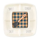 A white Mud Pie divided ceramic serving tray with four sections labeled "SWEET," "CRUNCHY," "SALTY," and "SAVORY." In the center is a stack of blue and brown plaid napkins and a wooden-handled spoon with a gray silicone head that reads "ENJOY."