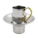 A hammered silver stainless steel cup with a gold, textured handle, resting on a matching hammered saucer and base.