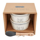 A Mud Pie bistro set packaged in a brown box. The set contains two stackable white ceramic bowls with gray stripes labeled 'GUAC' and 'SALSA', and a wooden spoon with a gray silicone end.