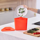 A two-tiered stainless steel trash and recycling bin with a black lid and base. The top compartment has a small, horizontal orange light on its front.