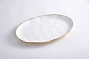 A large, oval white porcelain serving platter with a thin, irregular gold-painted rim and a wavy, organic shape.