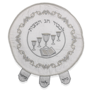 A round, white fabric matzah cover with intricate silver embroidery. The design features five wine cups, a book, and Hebrew text. The edge has a braided cord trim and three tabs.
